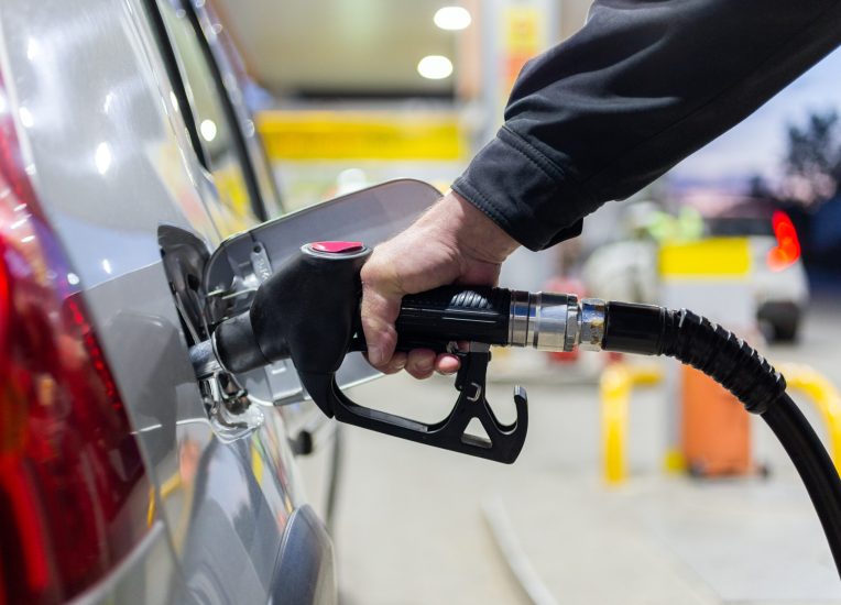 granddad's hand in black jacket refueling gray metallic car on gas station at night - close-up with selective focus and background blur